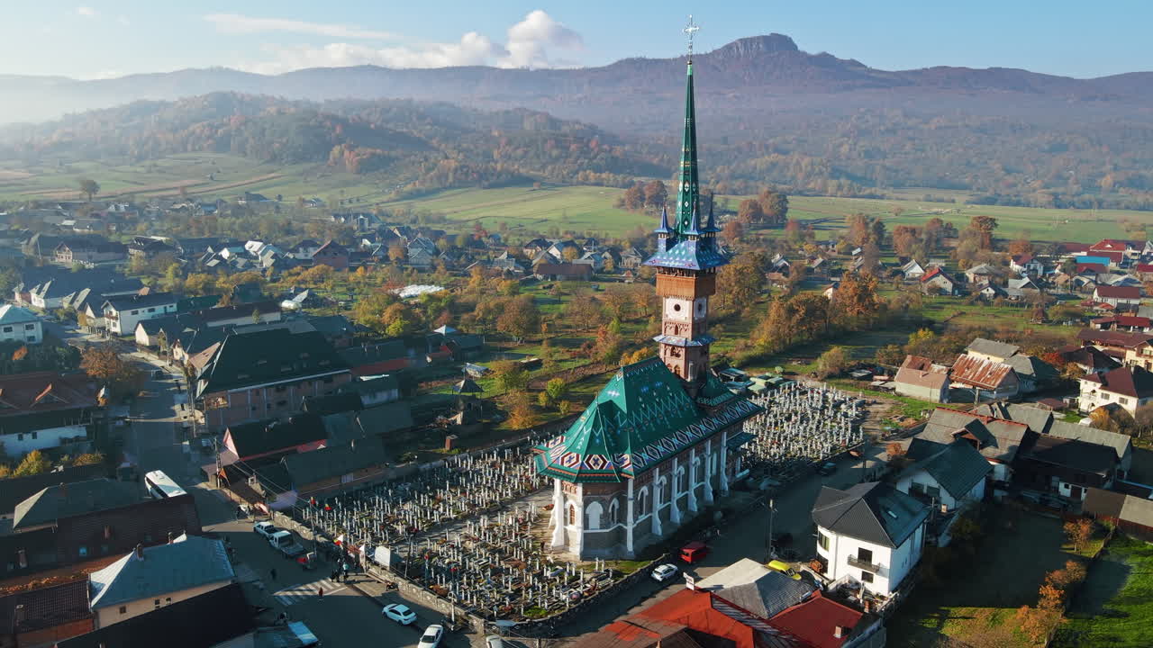 Aerial drone view of The Merry Cemetery in Sapanta, Romania. Church and multiple tombstones, visitors, residential buildings, yellowing trees