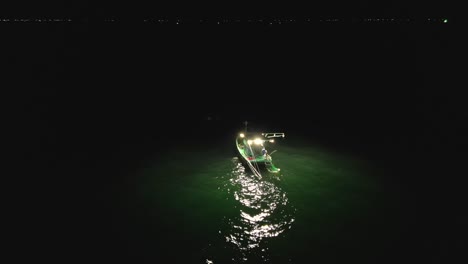 lone squid fishing boat illuminates the dark waters of phu quoc, vietnam, creating a captivating scene of nighttime activity, drone orbiting shot