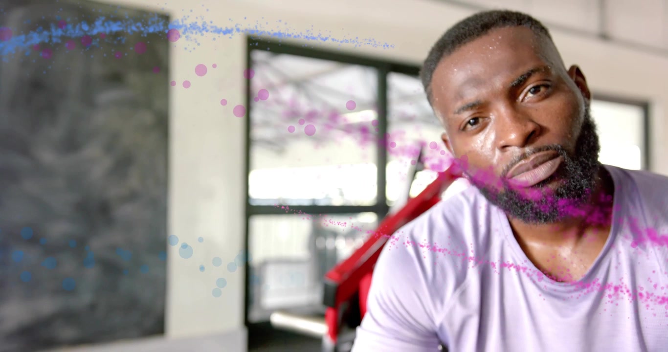 Man pausing between exercises on bench in gym, initiating pink blue particles drifting across lens