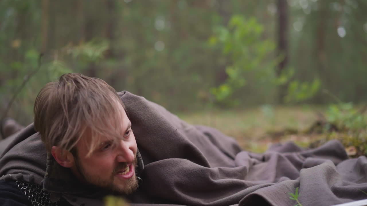 중세 시대의 체인 메일에서 부상을 입은 전사가 나무에 떨어집니다.