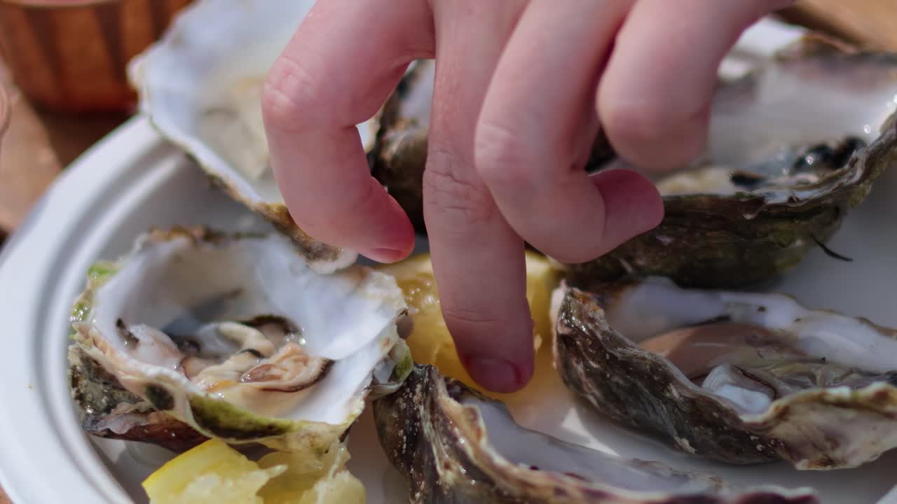 Close-up of oysters on a plate with a hand squeezing lemon over them.