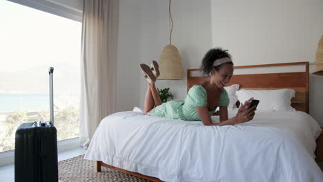 woman relaxing on bed, using smartphone, suitcase nearby, enjoying vacation, at home