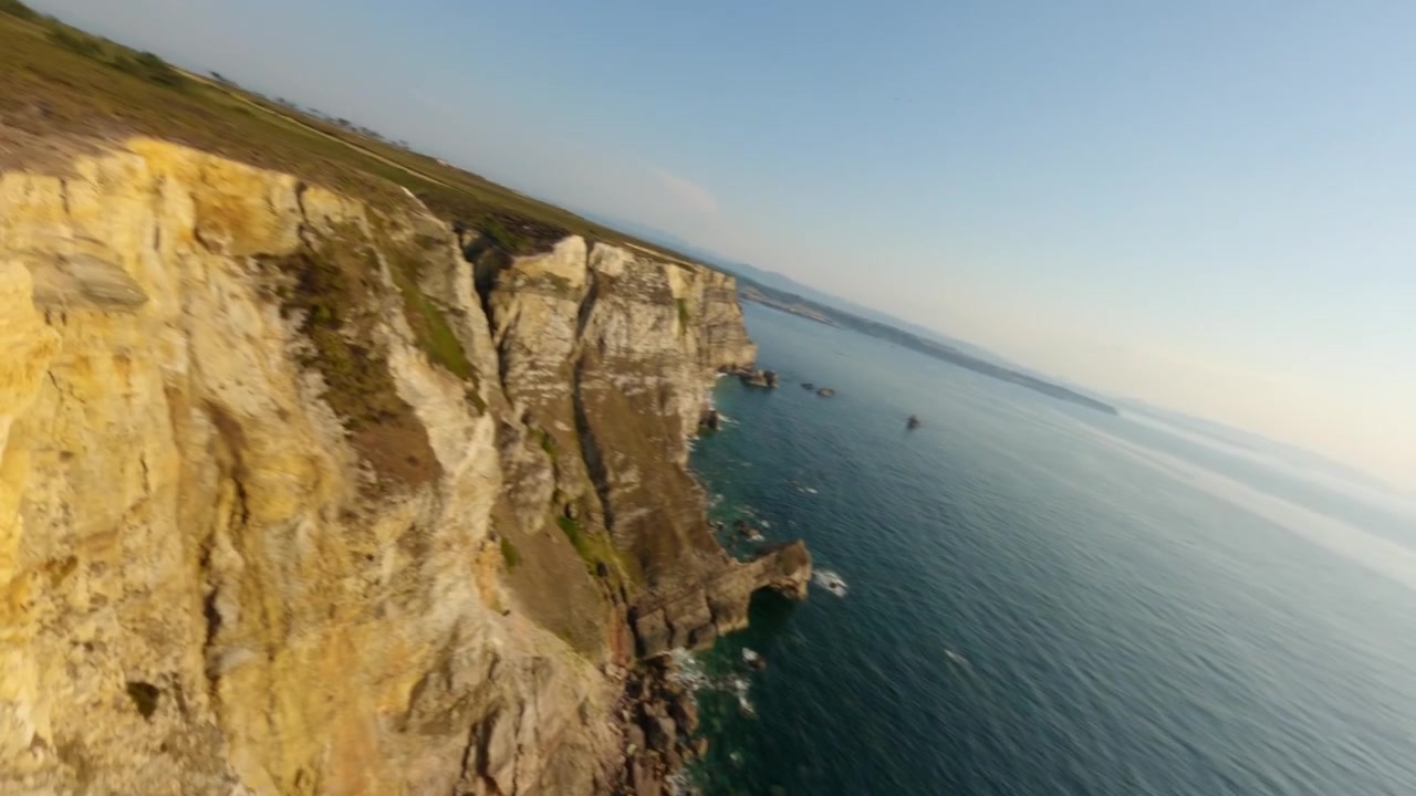 Dynamic aerial FPV drone footage soaring over the rugged limestone cliffs of Cabo Penas, the northernmost point of Asturias, Spain, overlooking the Cantabrian Sea at sunset.