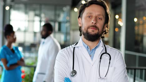 portrait of caucasian physician wearing a white gown looking at camera, smiling and standing in clinic