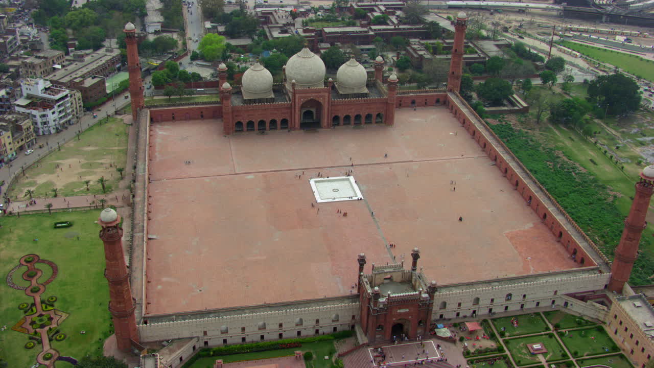 lahore, pakistán, vista aérea superior rotacional y alejada de la mezquita badshahi, rodeada de parques, visitantes damas, caballeros y niños están en la mezquita, fieles en el suelo de la mezquita