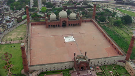 lahore, pakistan, top aerial rotational and zoom out view of badshahi mosque, surrounded by parks, visitors ladies, gents and children are in the mosque, worshipers in the ground of the mosque