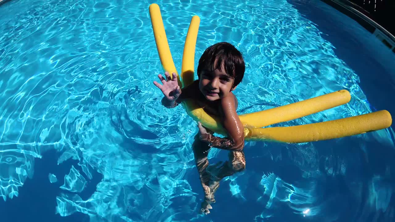 Happy Young Boy Floating in Swimming Pool with Yellow Noodles