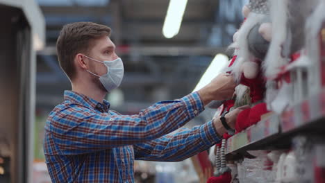 Un-Hombre-Con-Una-Máscara-Protectora-En-Una-Joyería-Y-Guirnaldas-Con-Juguetes-Para-árboles-De-Navidad-Y-En-Casa.-Guirnaldas-Navideñas-Y-Decoración