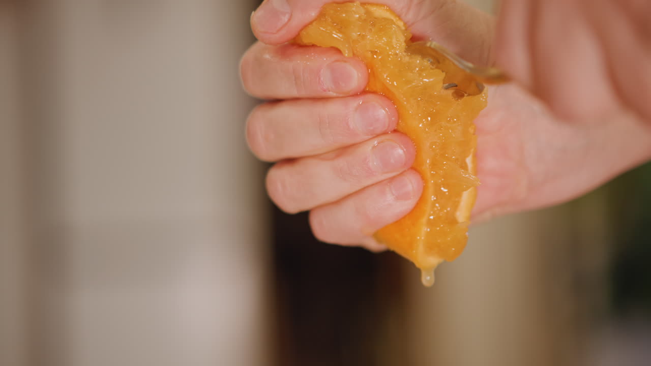 Manos recogiendo jugo de pulpa de cítricos. Toma de estudio capturando manos exprimiendo naranja para jugo fresco. Escena de estudio enfocada mostrando manos extrayendo pulpa y recogiendo jugo de cítricos en un recipiente.
