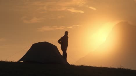 Man-climbing-out-of-a-mountain-tent-during-sunrise