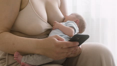 Unrecognizable-Mother-Breastfeeding-Her-Newborn-Baby-And-Using-Mobile-Phone-While-Sitting-On-The-Bed-At-Home-1