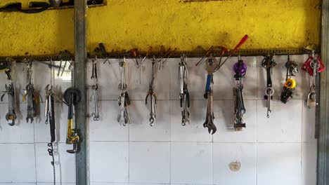 selection of bike tools including spanners, wrench and screwdrivers hanging against well worn, rustic yellow wall in bicycle repair shop