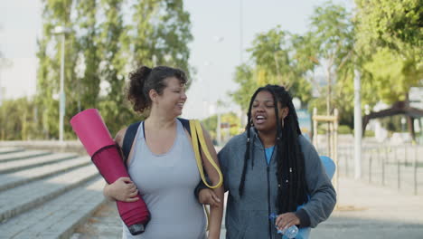mujer feliz en ropa deportiva caminando de brazos cruzados con un amigo