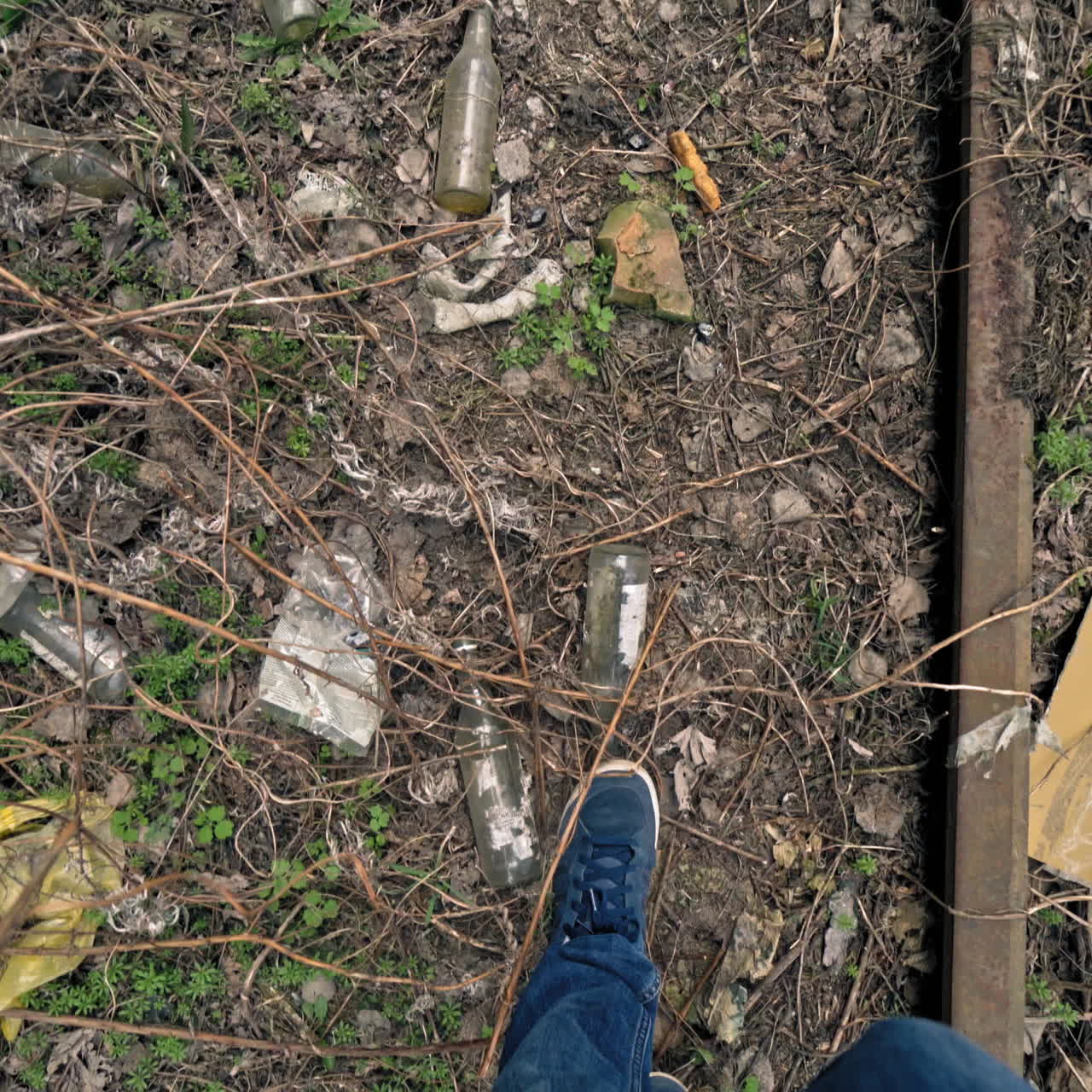 Man's legs walking on the dirty ground with many garbage outdoors. Male's feet stepping along the dirty place with glass bottles and rubbish.