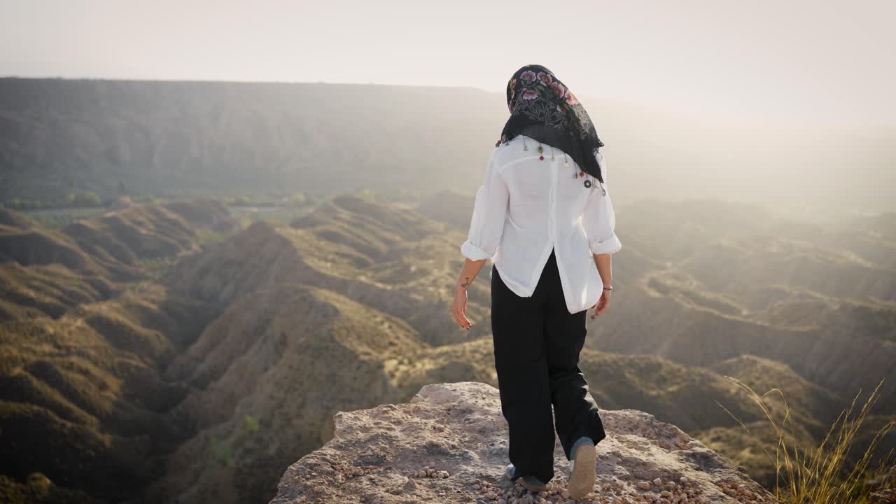 Woman traveler walking on mountain edge at sunset