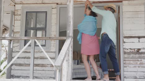 una pareja caucásica se divierte feliz bailando en el porche de una casa de playa de madera, en cámara lenta.