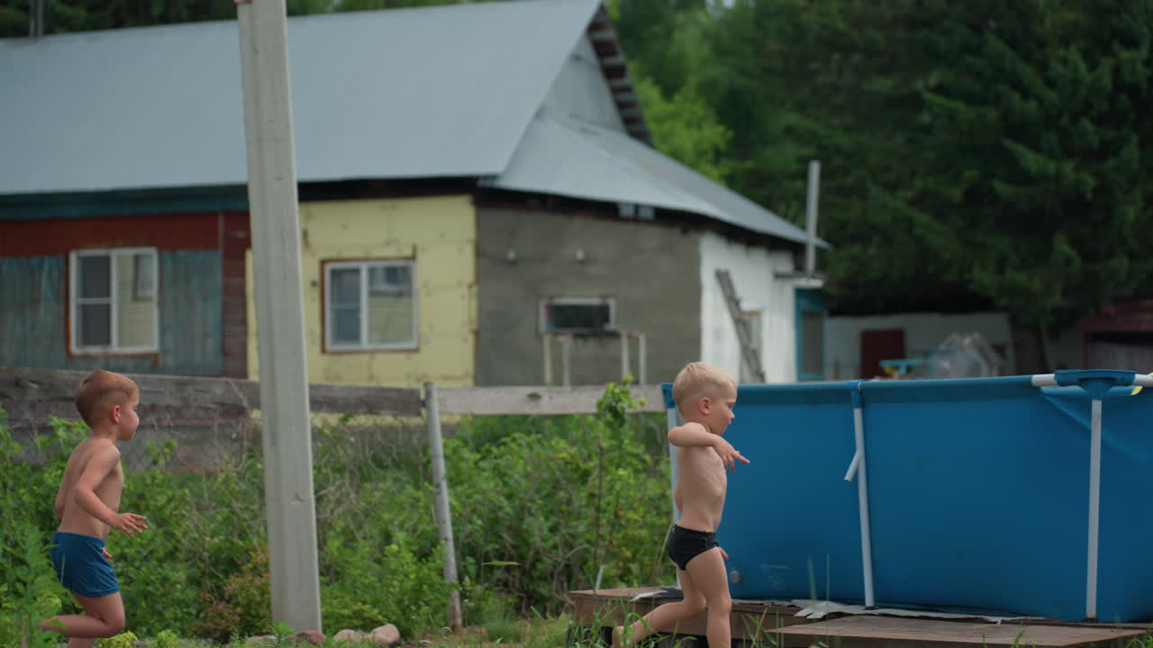 Laughter Echoes As Children Sprint Barefoot Outside, Young Girls And Boys Race Across Sunny Backyard Amidst Greenery, Girl Leads As Younger Boys Follow Near Greenhouse In Joyful Summer Chase