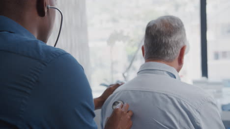 doctor listening to senior male patient breathing with stethoscope during medical exam in office