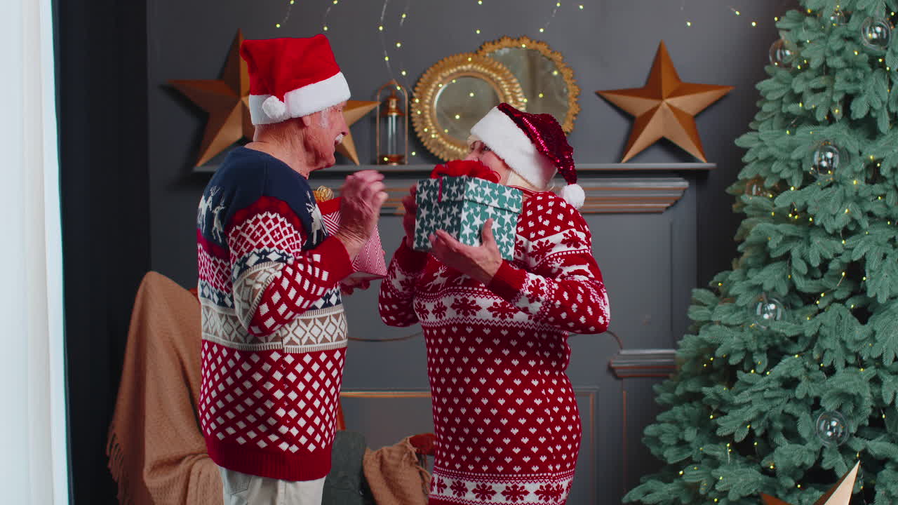 una pareja de ancianos románticos que se presentan cajas de regalos entre sí en casa cerca de la decoración del árbol de navidad