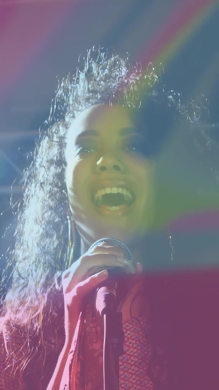 Video verticale: Cantante donna che intona la prima nota, afferrando il microfono, scuotendo i capelli, luci al neon che alimentano la musica.