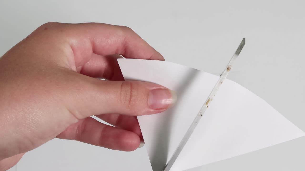 Close-up of hands folding and cutting white paper with scissors, demonstrating precision and technique.