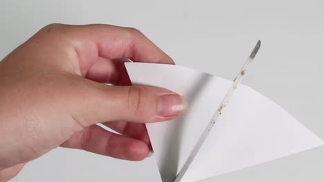 close-up of hands folding and cutting white paper with scissors, demonstrating precision and technique.
