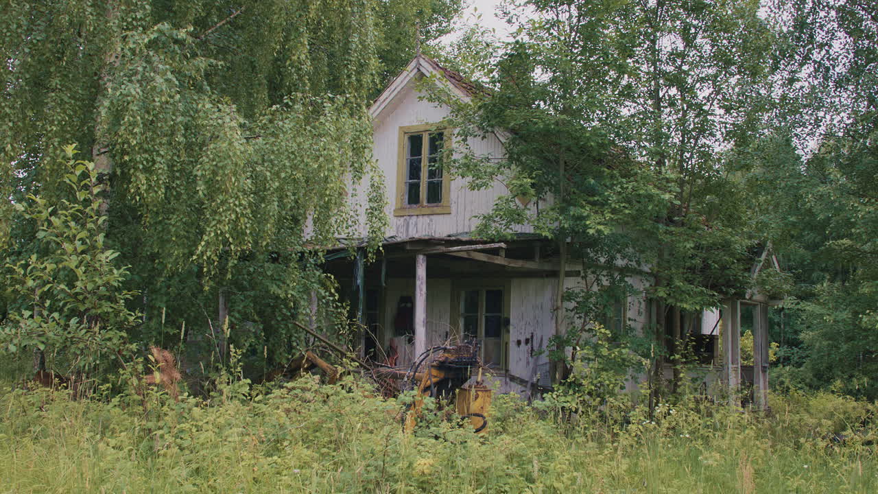 Abandoned wooden house surrounded by lush greenery, showing signs of decay and neglect.
