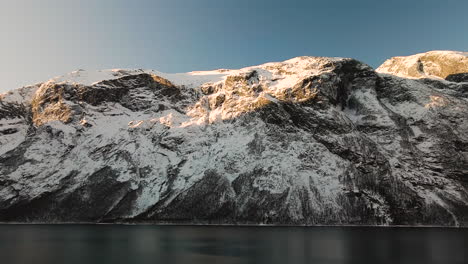 Sunlight-On-Snow-Forest-Mountains-By-The-Calm-Shore-During-Winter-In-Norway