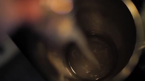 pouring liquor into stainless steel shaker to prepare alcohol cocktail, close up