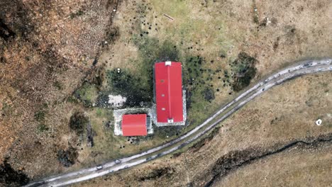 A-drone-slowly-twists-and-rises-above-the-red-roof-of-a-remote-bothy-in-the-highlands-of-Scotland-in-winter