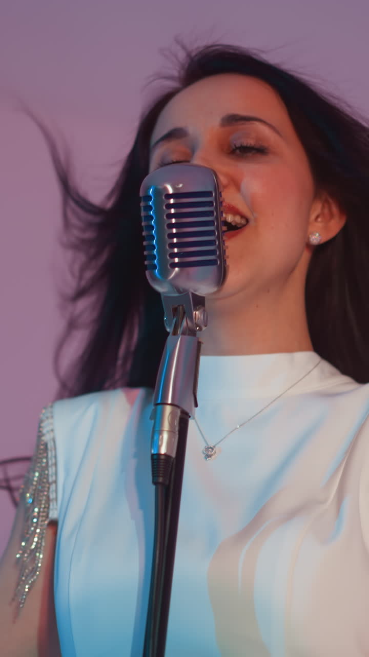 색 드레스를 입은 여성 가수가 손을 들어 머리를 뒤로 펴고 열정적으로 노래하며 회색 배경에 깊은 감정을 표현합니다.