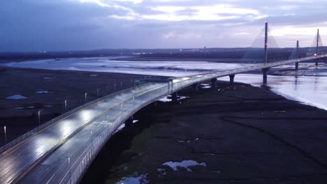 Aerial-view-Mersey-gateway-illuminated-freeway-bridge-overpass-lanes-early-morning-sunrise-slow-reverse