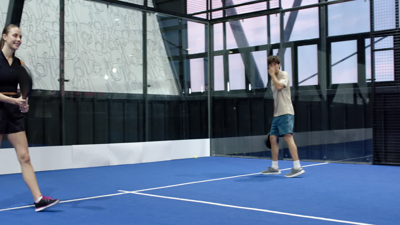 Young woman playing padel tennis on indoor court, smiling and holding racket energetically