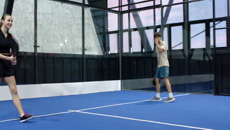 young woman playing padel tennis on indoor court, smiling and holding racket energetically