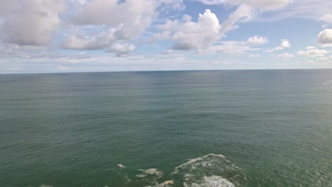 Aerial-dolly-in-rising-over-rocky-shore-and-turquoise-sea-on-a-cloudy-day-in-in-Dominicalito-Beach,-Costa-Rica