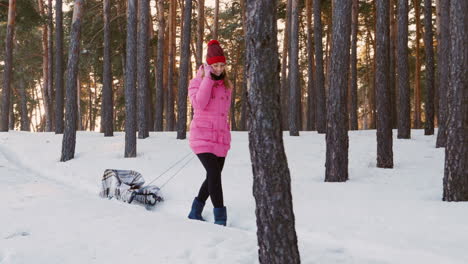 Young-Woman-In-Pink-Down-Jacket-Carries-A-Empty-Sled-In-The-Winter-Woods-1