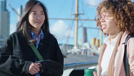 two young women standing on city riverbank and chatting