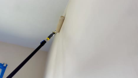 Low-Angle-Looking-Up-at-Paint-Roller-Coating-White-Walls-in-Fresh-Paint,-Painter's-Pole-Rolling-Fresh-Paint-onto-White-Wall-beside-Window