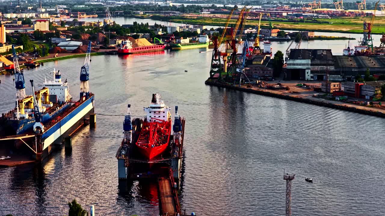 A slow aerial orbit reveals a busy shipyard in the Port of Riga, showing ships in both a dry dock and a floating dock for repair and maintenance, surrounded by cranes and industrial facilities