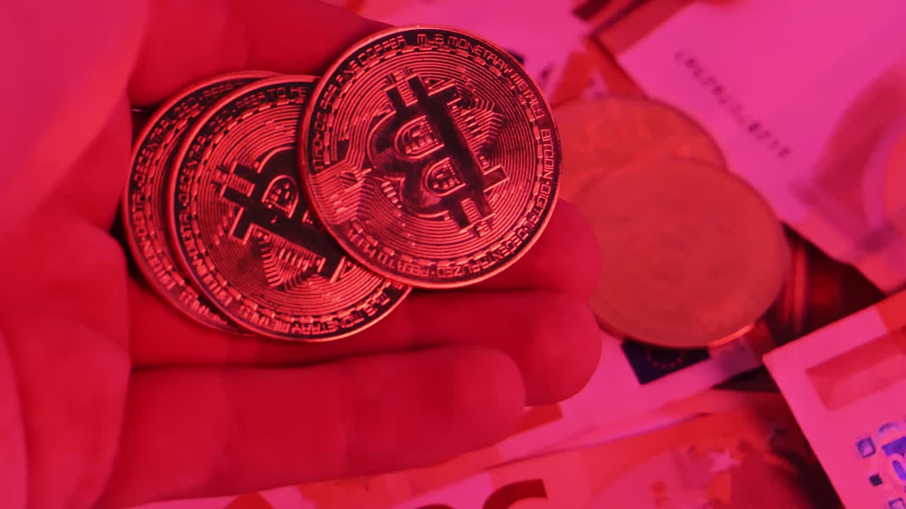 Primo piano di monete bitcoin dorate illuminate di rosso sopra banconote da cinquanta euro rotanti