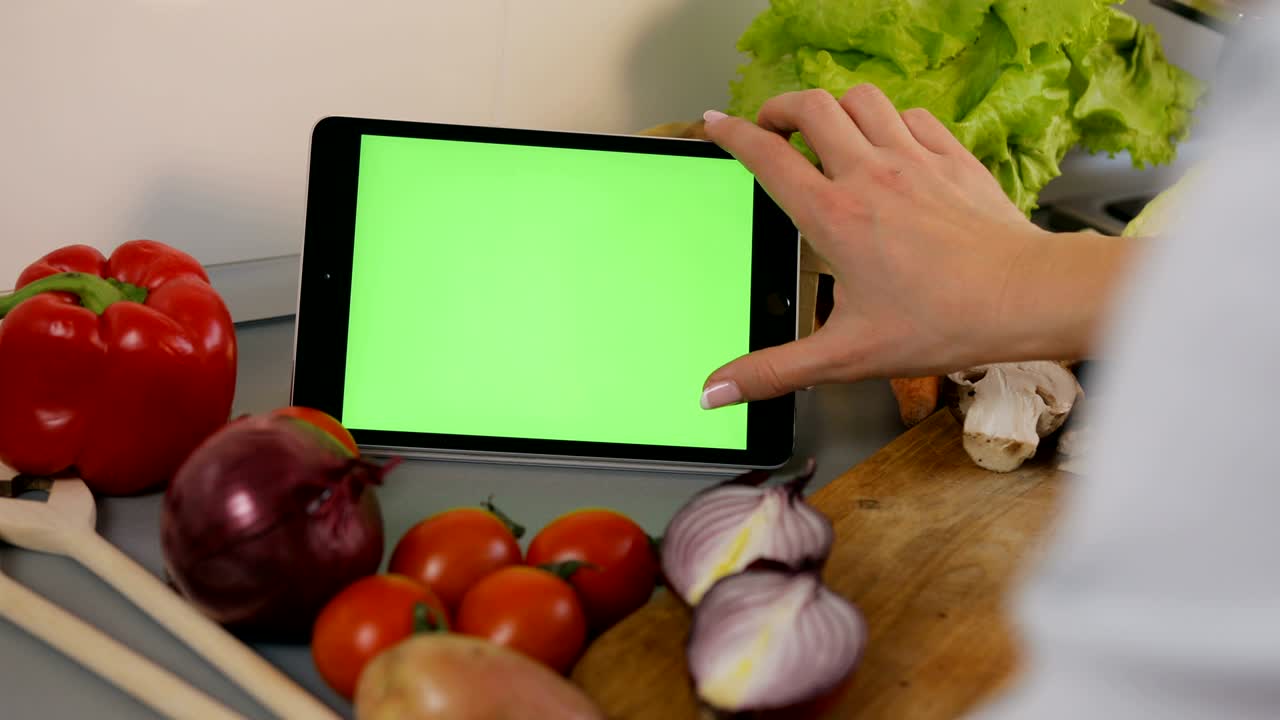 mujer joven desplazándose a través de recetas en su tableta en la cocina