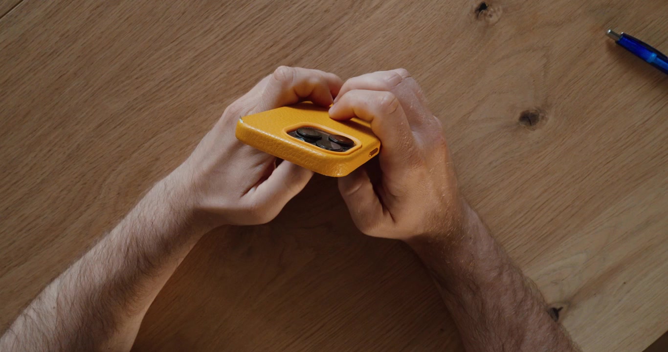Top-down view of a person holding and using a smartphone on a wooden table. Mobile technology, communication, everyday lifestyle, and digital device concept.