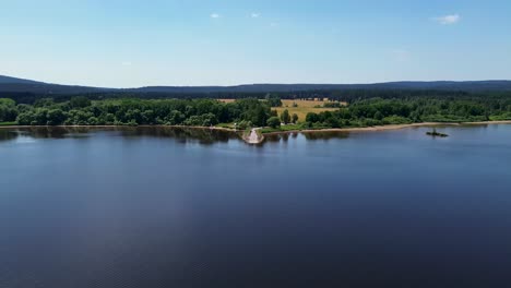 cinematic drone view as it flies over a large blue lake and heads towards land