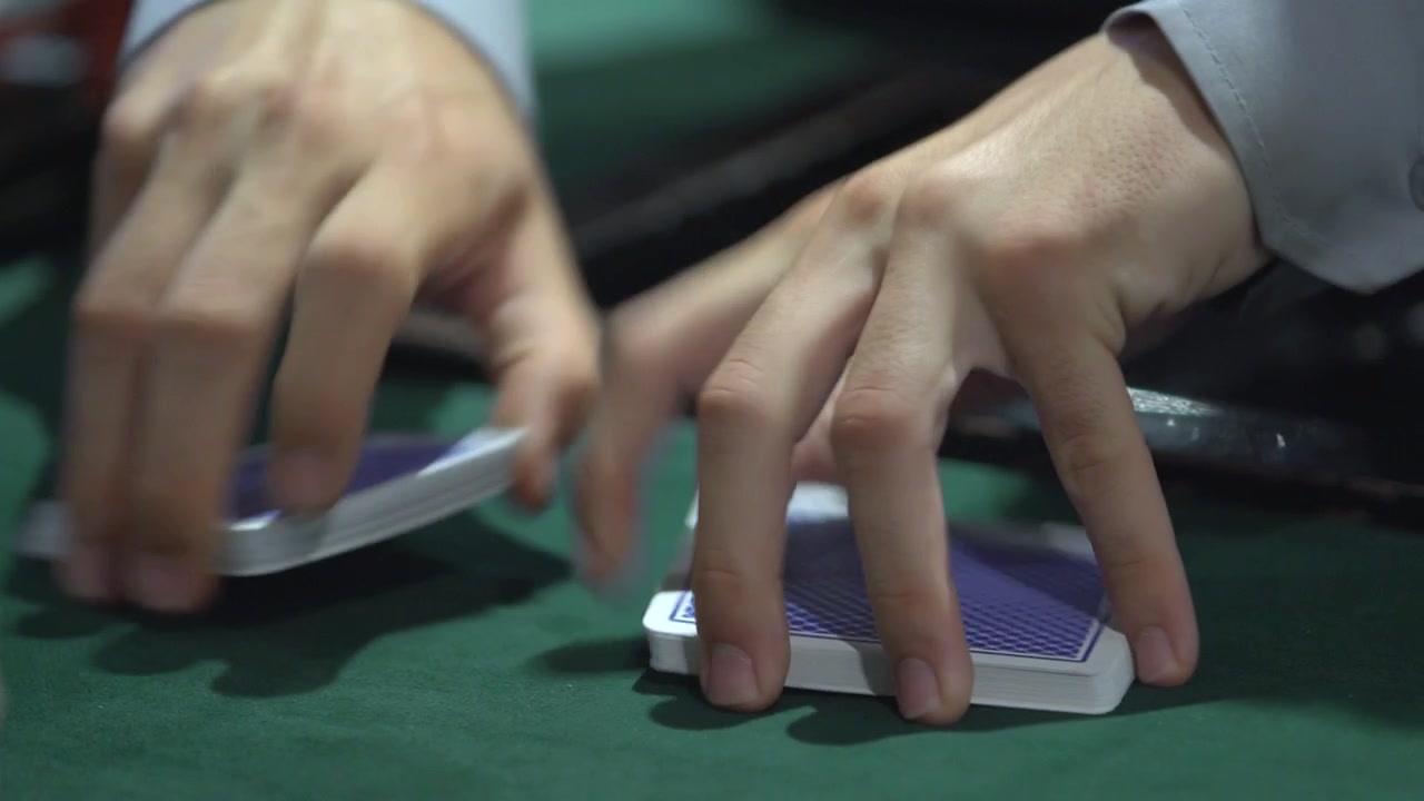 Plano detalhe de cartas de póquer sendo baralhadas por um croupier de casino. Filmagem de jogo, mesa de casino, jogo de cartas e ambiente de vida noturna.