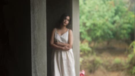 Young-Indian-woman-in-a-white-dress-stands-pensively-by-a-wall,-transitioning-from-a-blurry-to-a-clear-shot