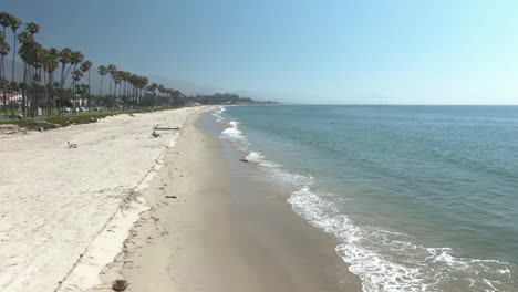 Cinematic-horizontal-moving-aerial-of-beautiful-empty-beach-with-small-waves-and-palm-trees-in-Santa-Barbara,-California,-USA