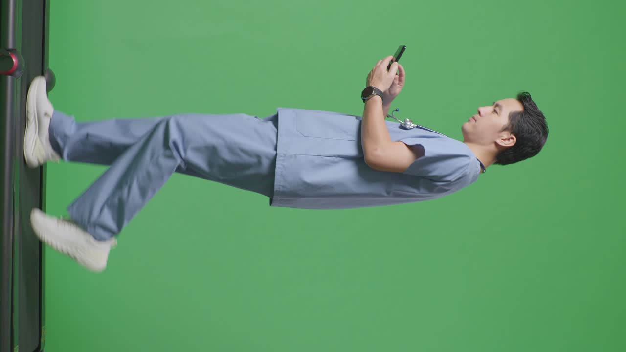 병원에서 녹색 화면 배경에서 는 동안 스마트폰을 사용하여 스테토스코프를 가진 아시아 남성 의사