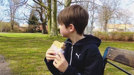 caucasian boy eating a sandwich outdoors and drinking an energy drink