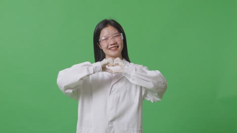 asian woman scientist smiling and showing shape heart with hands while standing on the green screen background in the laboratory