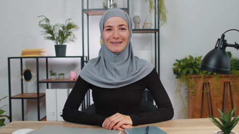 Businesswoman-working-smiling-friendly-at-camera-and-gesturing-hello-assalamu-alaikum-at-home-office